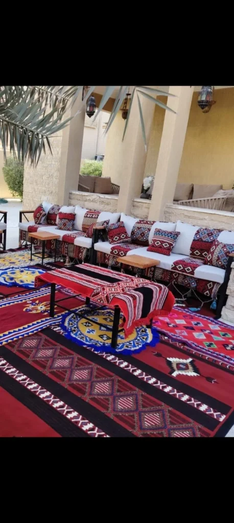 جلسة كنب بنقوش تراثية حمراء مع سجاد وطاولات ضيافة في مساحة خارجية.