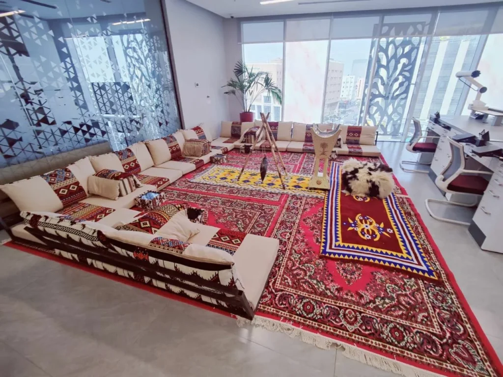 كنب مجلس بنقوش حمراء وبيضاء حول سجاد تراثي وطاولات ضيافة داخلية.